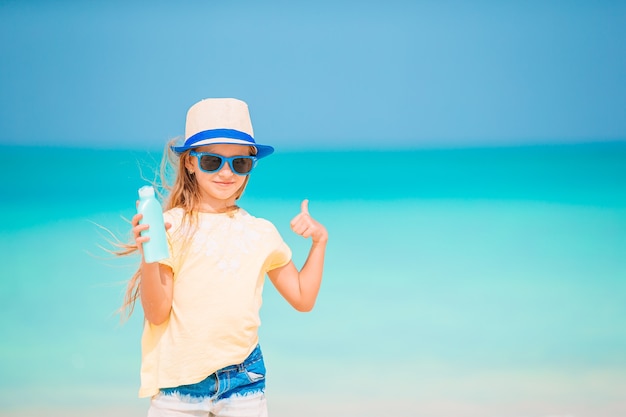 Beautiful little girl on the beach with sun cream bottle. Sun protection