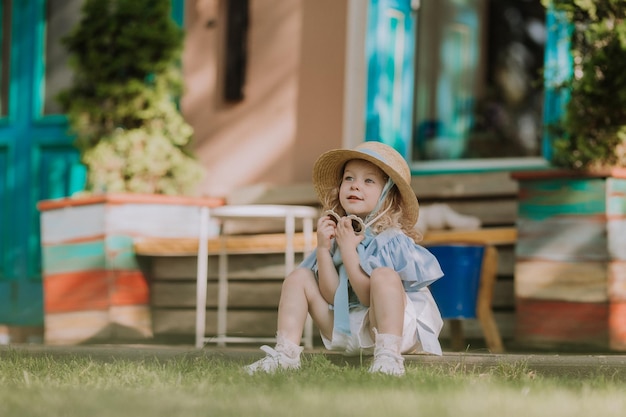 beautiful little girl in blue dress, straw hat and sunglasses playing outdoor, blue background, card