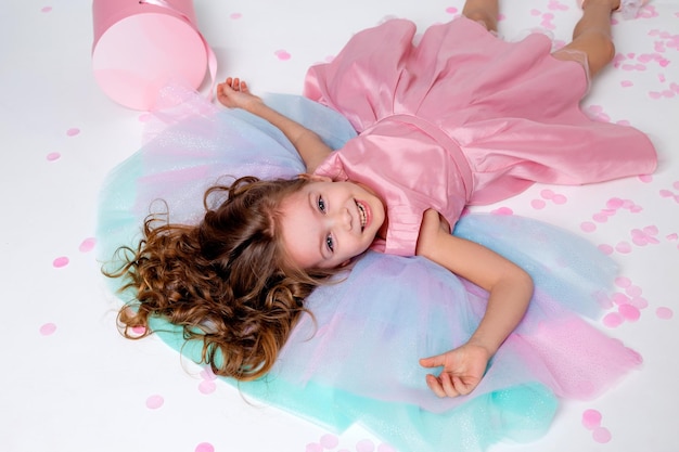 Beautiful little girl in a chic pink dress lies on the floor strewn with confetti top view