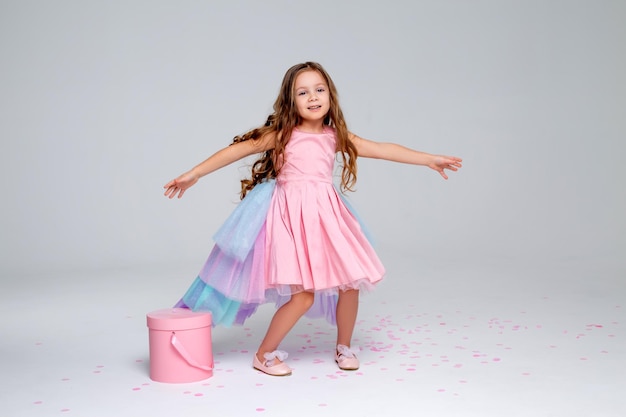 Beautiful little girl in a chic pink dress poses standing and holds a hatbox in her hands