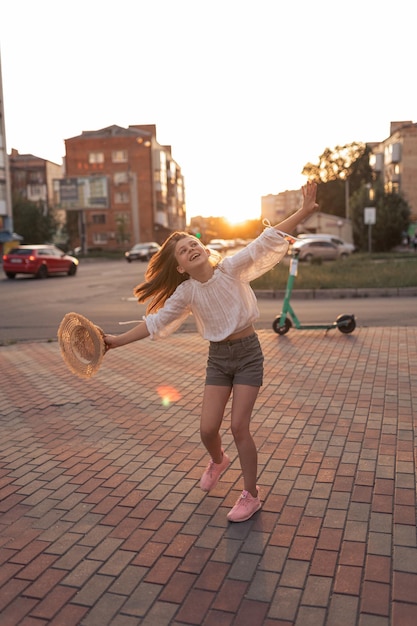 Beautiful little girl in the city at sunset A girl in a white blouse and with a straw hat is having fun outside recreation