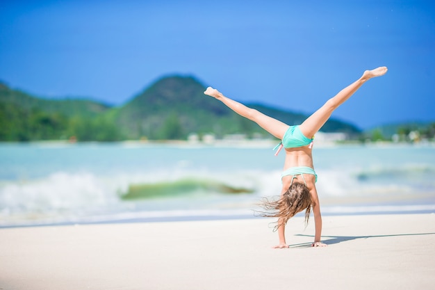 Beautiful little girl doing sporty exercises on the beach