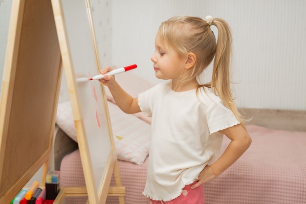 beautiful little girl at home draws with felt-tip pen on the blackboard