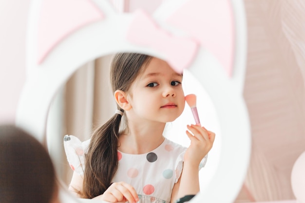 A beautiful little girl in the mirror preening a little girl is sitting at a children's table and is wearing children's cosmetics