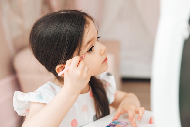 A beautiful little girl in the mirror preening a little girl is sitting at a children's table and is wearing children's cosmetics