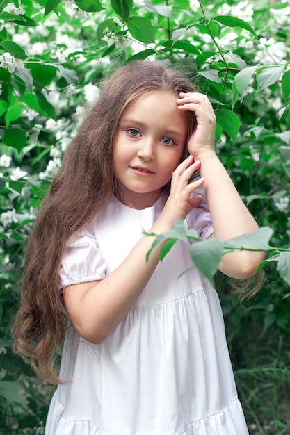 A beautiful little girl poses with a large bouquet of flowers in a luxurious white dress in a city park