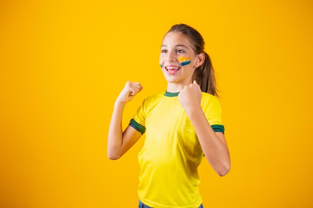 Beautiful little girl rooting for her team on yellow background. Little girl celebrating the goal and celebrating Brazil's victory