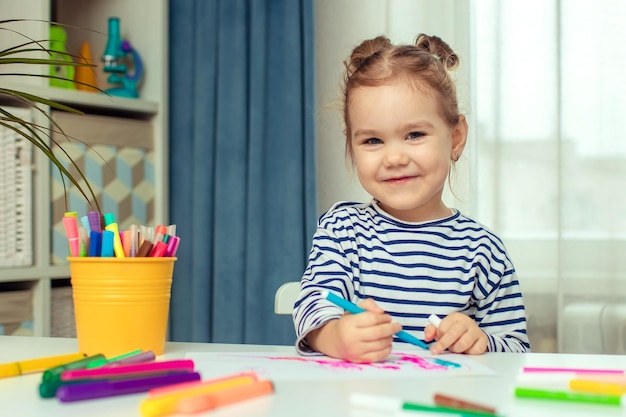 A beautiful little girl sits at a table at home and draws Development of preschoolers