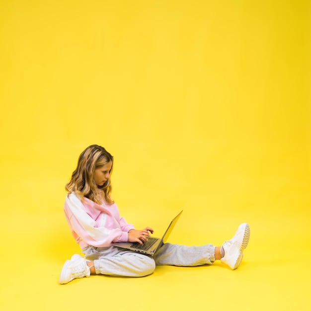 Beautiful little girl sitting on a light floor with a gray laptop and smiling empty space