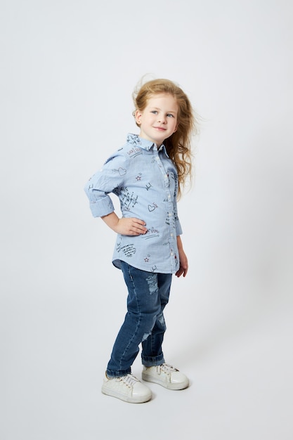 Beautiful little girl smiles, child in autumn clothes poses on a white wall