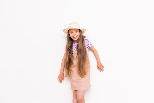 A beautiful little girl in a sundress and a straw hat is getting ready for a summer vacation Summer holidays for children White isolated background