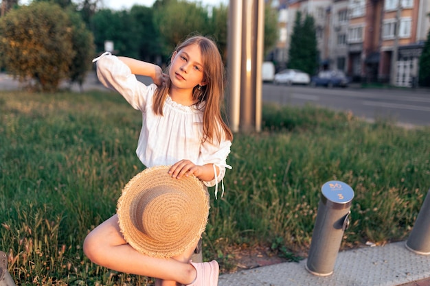 Beautiful little girl at sunset with a straw hat straightens her hair