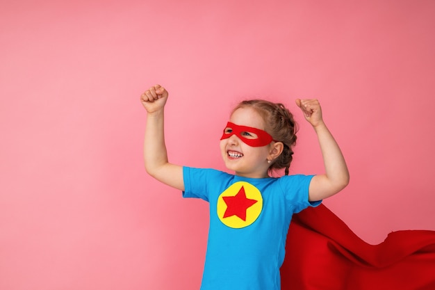 Beautiful little girl in superhero costume in red Cape and mask shows how strong