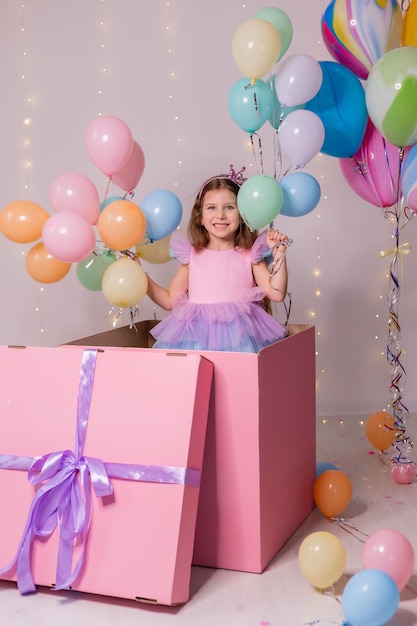 Beautiful little girl with balloons jumps out of a huge pink box child celebrates his birthday