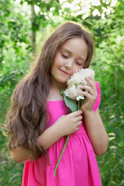 A beautiful little girl with a bouquet of peonies in her hands in a summer field Photo shoot in the spring garden under the open sky