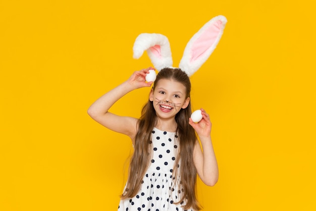 A beautiful little girl with fur rabbit ears on her head holds chicken eggs in her hands to paint them for the Easter holiday