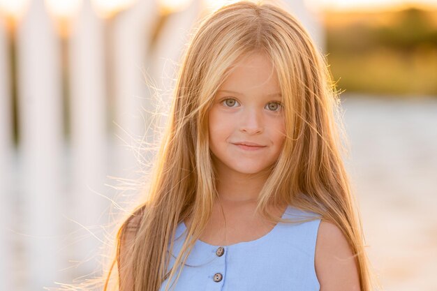 beautiful little girl with long blonde hair walks at sunset in the city park in summer