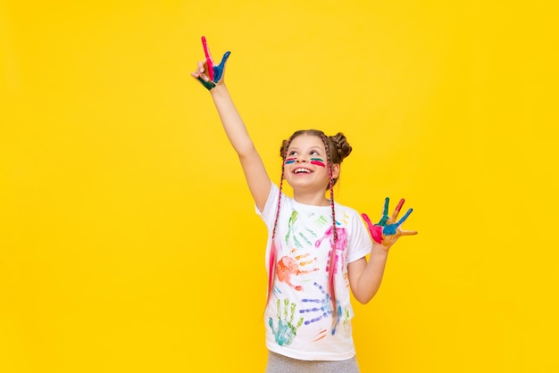 A beautiful little girl with stained hands in paint points her fingers in different directions A child in paint on a yellow background