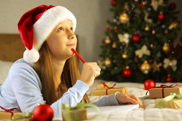 Beautiful little girl writing a letter to santa claus in the christmas interior