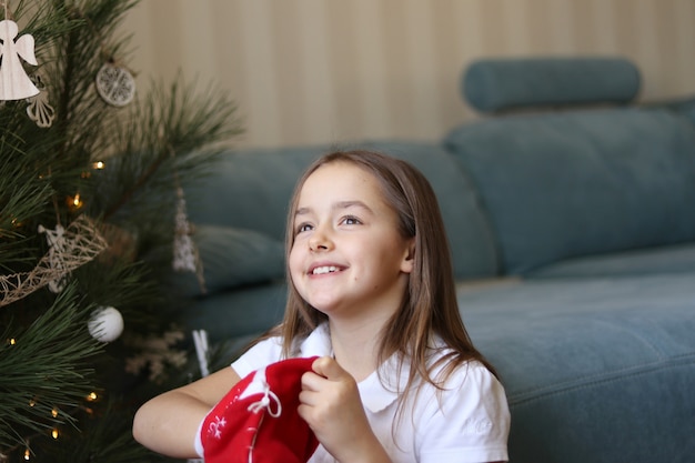 Beautiful little smiling girl taking Christmas gifts out of red traditional bag with hope 