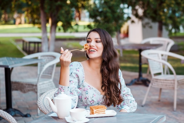 Beautiful long haired woman eating honey cake in the outdoor cafe in summer