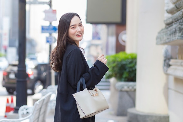 Beautiful longhaired Asian woman in a black coat carrying a walking bag smiling in a good mood