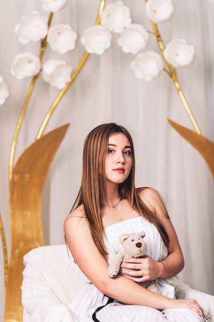 Beautiful longhaired girl with a teddy bear in his hands on a floral background