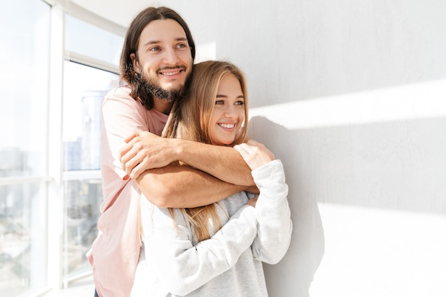 Beautiful lovely couple standing at the living room at the window, hugging