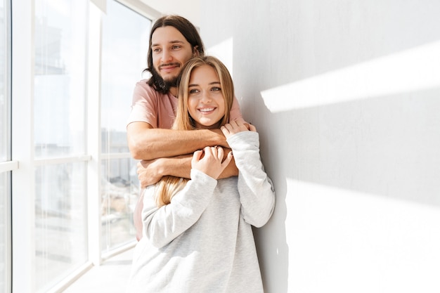 Beautiful lovely couple standing at the living room at the window, hugging