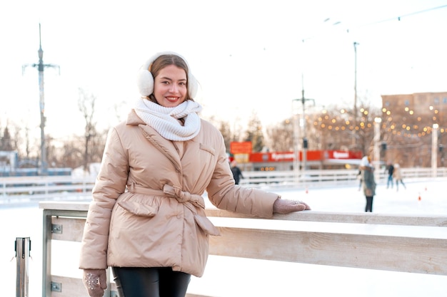 Beautiful lovely young adult woman brunet hair warm winter jackets stands near ice skate rink background Town Square Christmas mood lifestyle