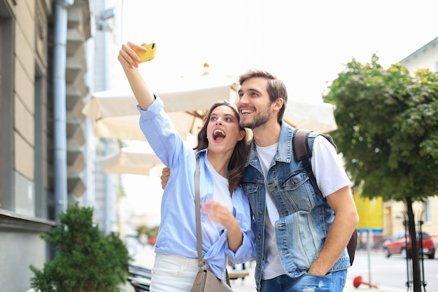 Beautiful lovely young couple walking at the city streets, hugging while taking a selfie.