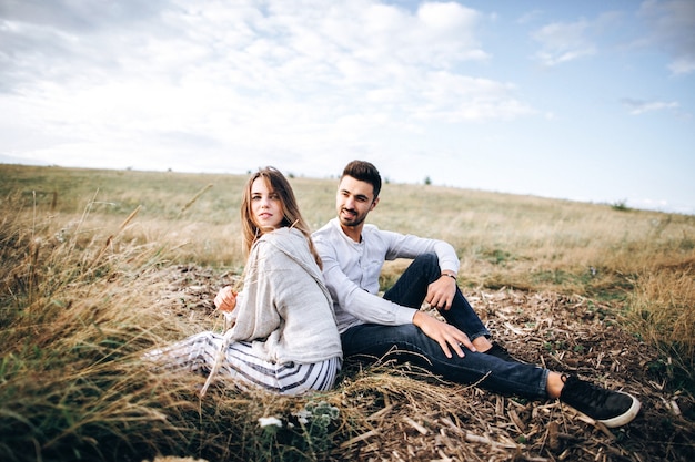 Beautiful loving couple sitting on grass. The guy and the girl hipster travel