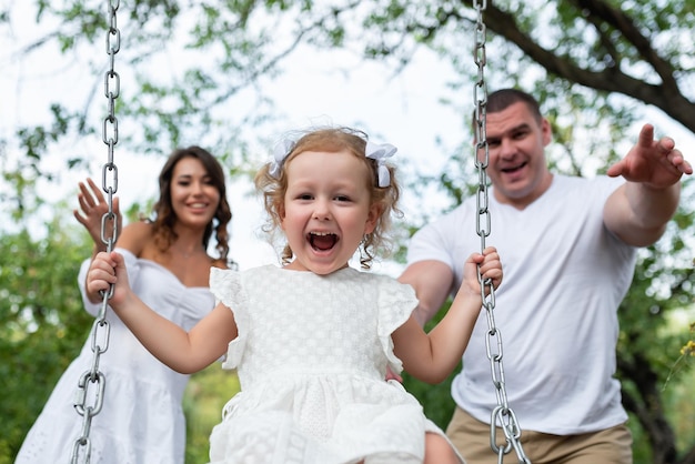 Beautiful loving family having fun outdoors Mom dad ride their daughter on a swing Parents with children ride on a swing Have fun and rejoice