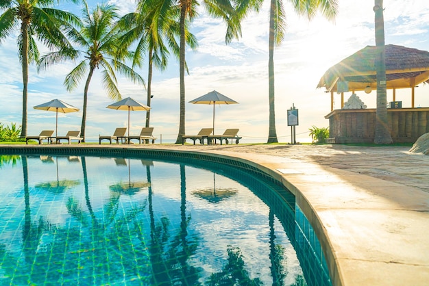 Beautiful luxury umbrella and chair around outdoor swimming pool in hotel and resort with coconut palm tree on sunset or sunrise sky