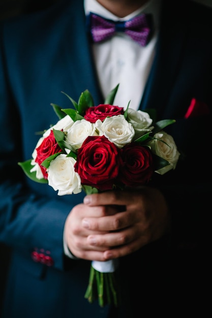 Beautiful man in a suit holding in hands festive bouquet of flowers. Gift to Women's Day. Agency floral design. Gift bouquet on March 8