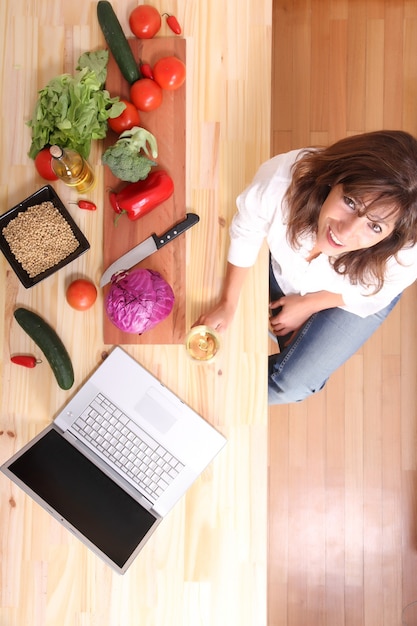 A beautiful mature woman cutting in the kitchen with the help of a computer.