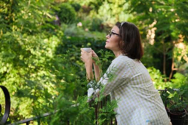 Beautiful mature woman in home clothes on open balcony with cup of coffee