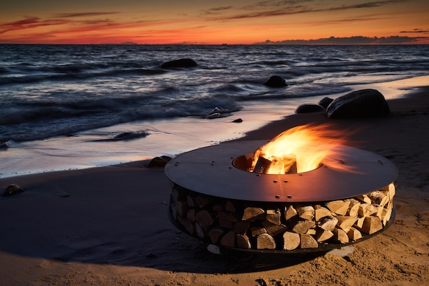 The beautiful metal round a fireplace stands on the sandy coast with a tidal wave at sunset stones s...