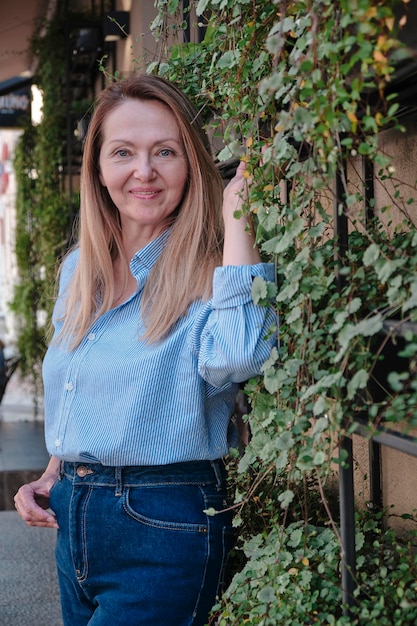 Beautiful middle age woman smiling cheerful leaning on a brick wall at the city street on a sunny day