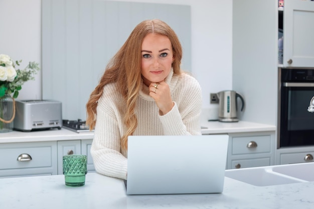 Beautiful middle age woman with laptop working from home online at her cozy kitchen