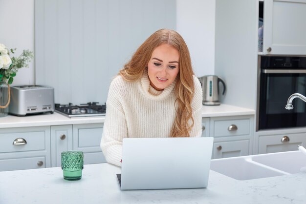 Beautiful middle age woman with laptop working from home online at her cozy kitchen