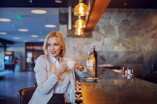 A beautiful middle-aged businesswoman sitting in a hotel cafe and enjoying her coffee. She waiting for a business meeting. Free time, enjoyment, respite, lifestyle