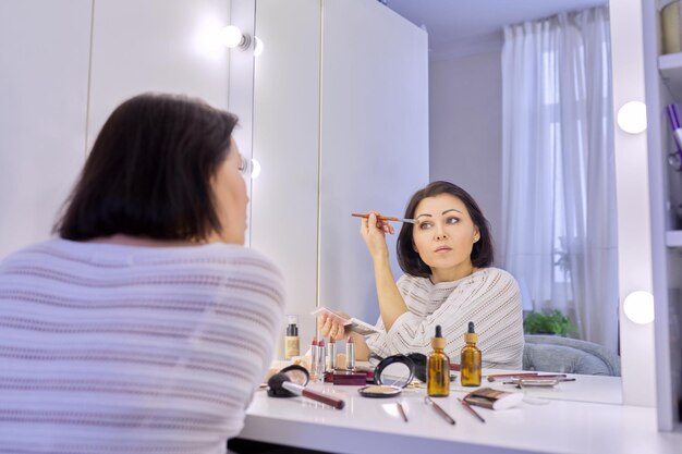 Beautiful middle aged woman doing makeup in front of a mirror