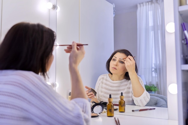 Beautiful middle aged woman doing makeup in front of a mirror