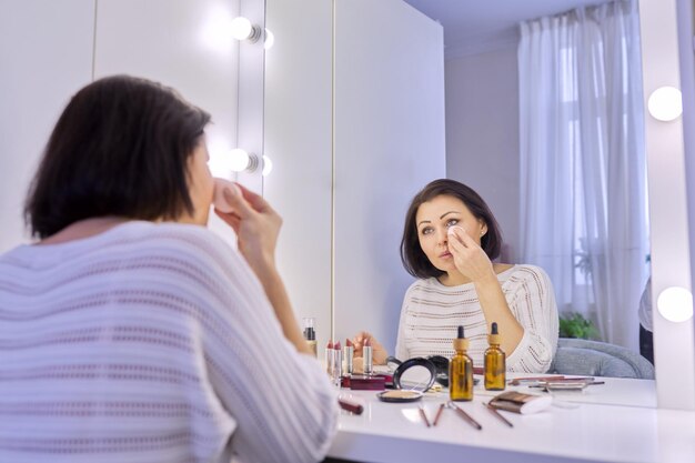 Beautiful middle aged woman doing makeup in front of a mirror