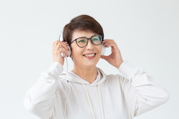 Beautiful middle-aged woman in light sweater and glasses is listening to her favorite music with wire headphones and high-speed Internet