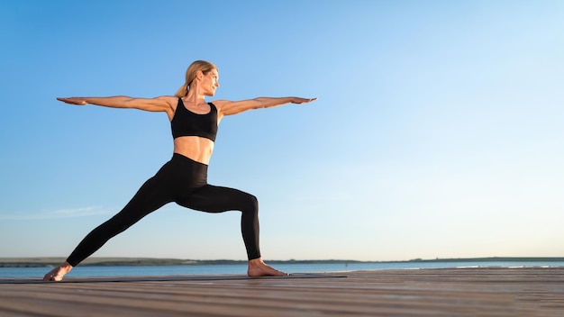 Beautiful Middle Aged Woman Practicing Yoga Outdoors Standing In Warrior Pose