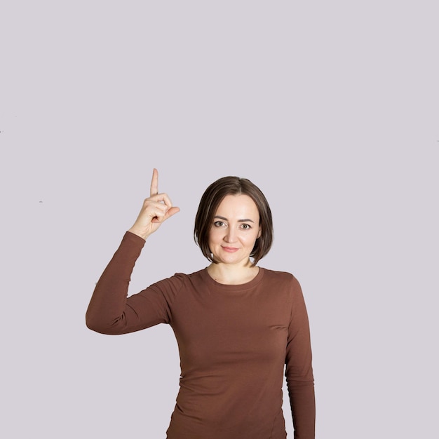 Beautiful middleaged brunette woman on a gray background points up