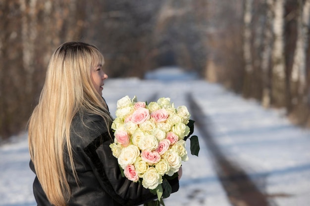 Beautiful middleaged woman with a bouquet of white roses in the winter forest