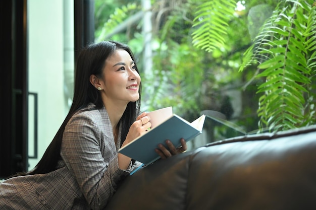 Beautiful millennial woman reading book while resting on couch at her office